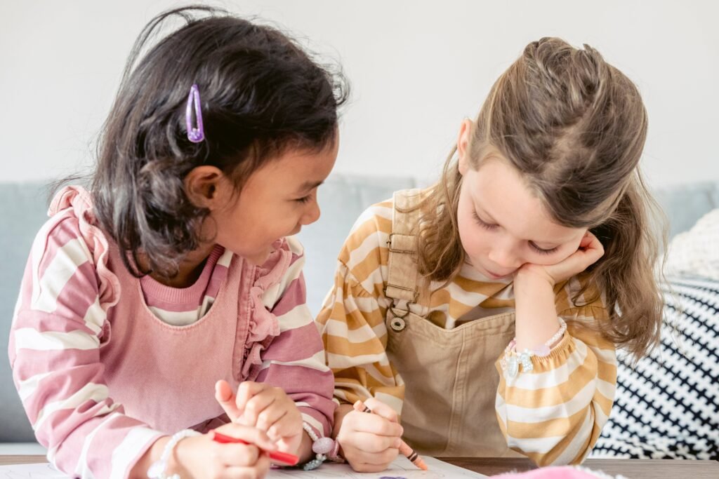 Two young girls are speaking to eachother while drawing with crayons